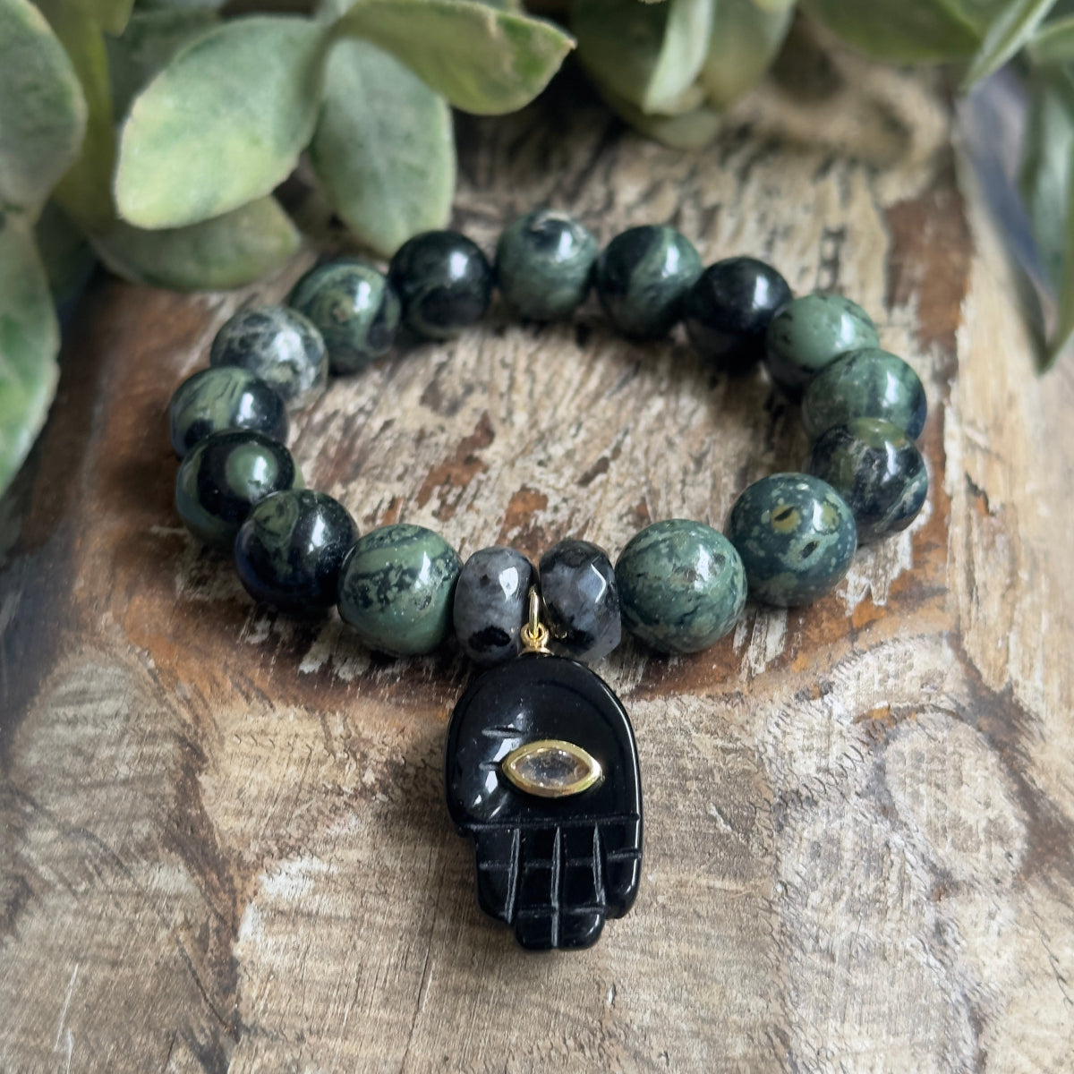 Lifestyle photo of a unisex 10mm genuine stone protection bracelet with green Kambaba Jasper and grey Larvikite beads worn on a wrist.