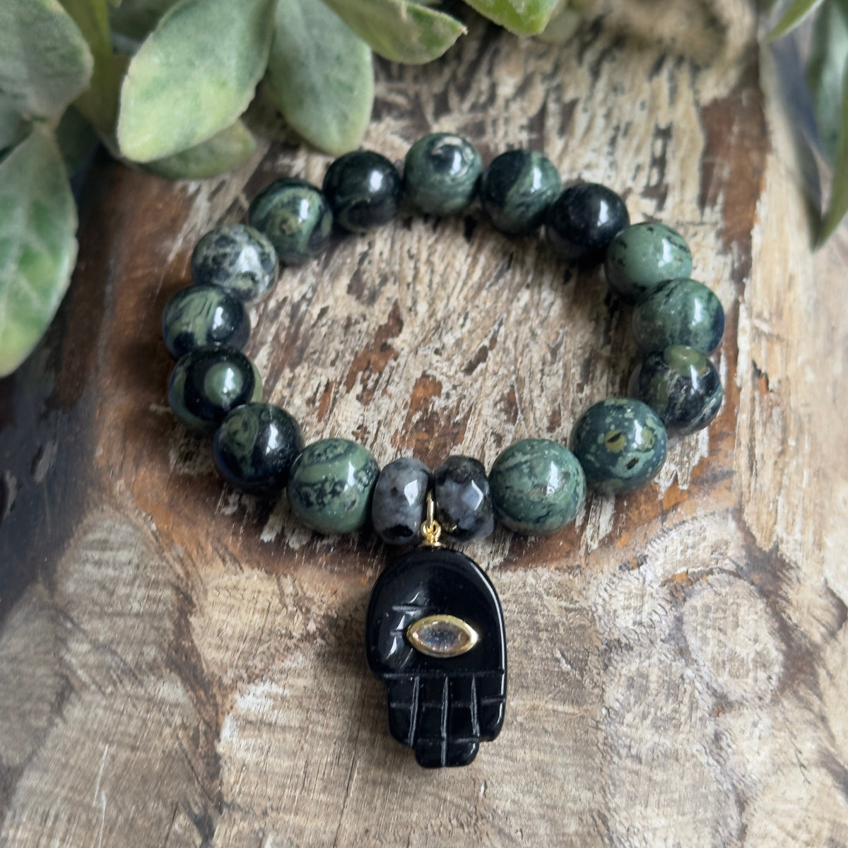 Close-up shot of a 10mm grounding gemstone bracelet highlighting the optional black onyx Hamsa hand charm and glittering CZ evil eye detail.