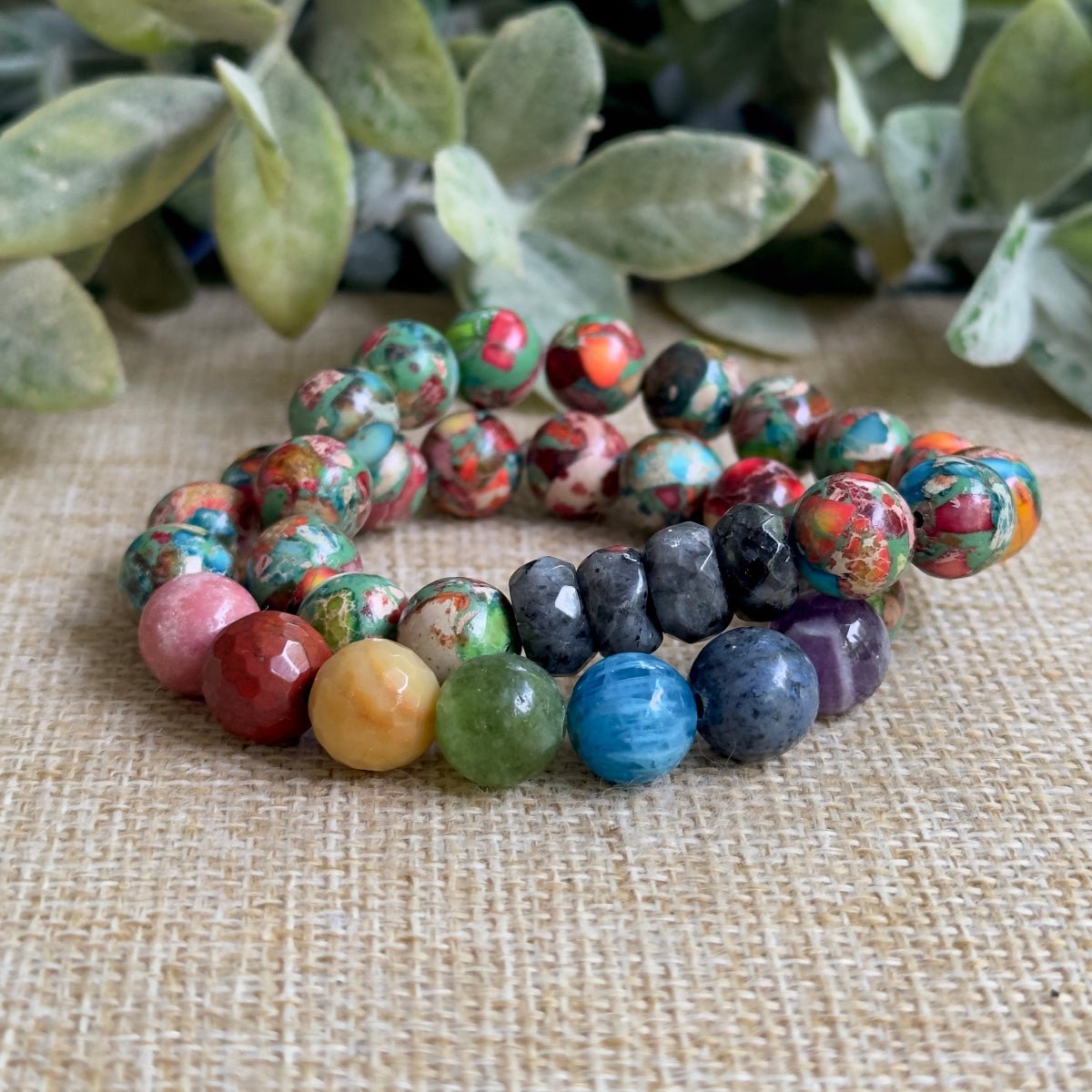 Close-up of a seven chakra mosaic bracelet showing smooth, round gemstone beads arranged in a vibrant rainbow color sequence with intricate wire wrapping details.